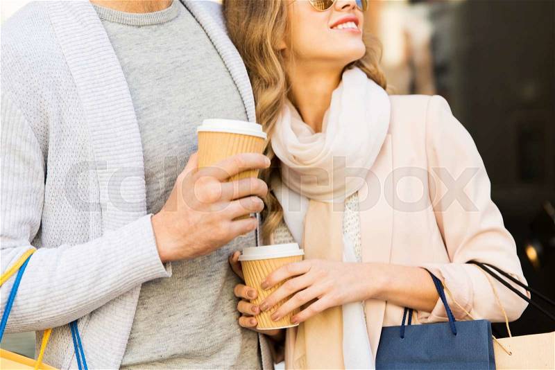 Sale, consumerism and people concept - close up of happy couple with shopping bags and coffee paper cups at shop window on city street, stock photo
