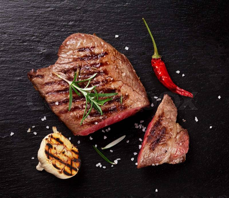 Grilled beef steak with rosemary, salt and pepper on black stone plate. Top view, stock photo