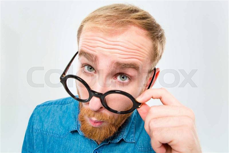 Closeup portrait of amusing young man with beard looking over black round glasses, stock photo
