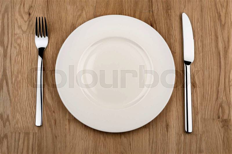 Plate, knife and fork on a wooden table with free space, stock photo