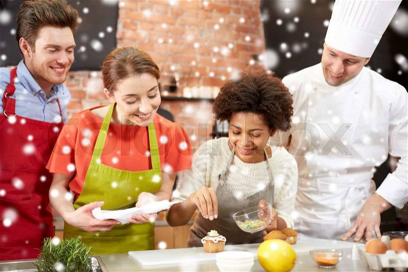 Cooking class, culinary, bakery, food and people concept - happy group of friends and male chef cook baking in kitchen over snow effect, stock photo