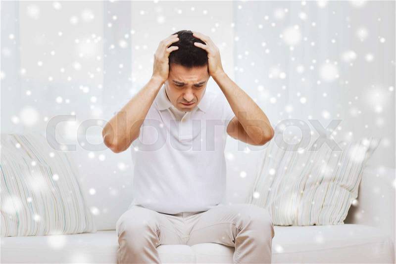 People, crisis, emotions and stress concept - unhappy man suffering from head ache at home over snow effect, stock photo