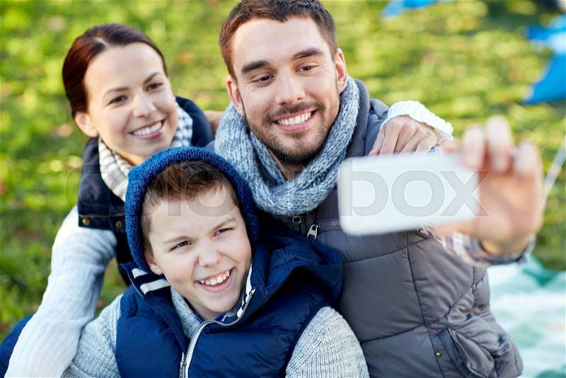 Camping, hike, technology and people concept - happy family with smartphone taking selfie at campsite, stock photo