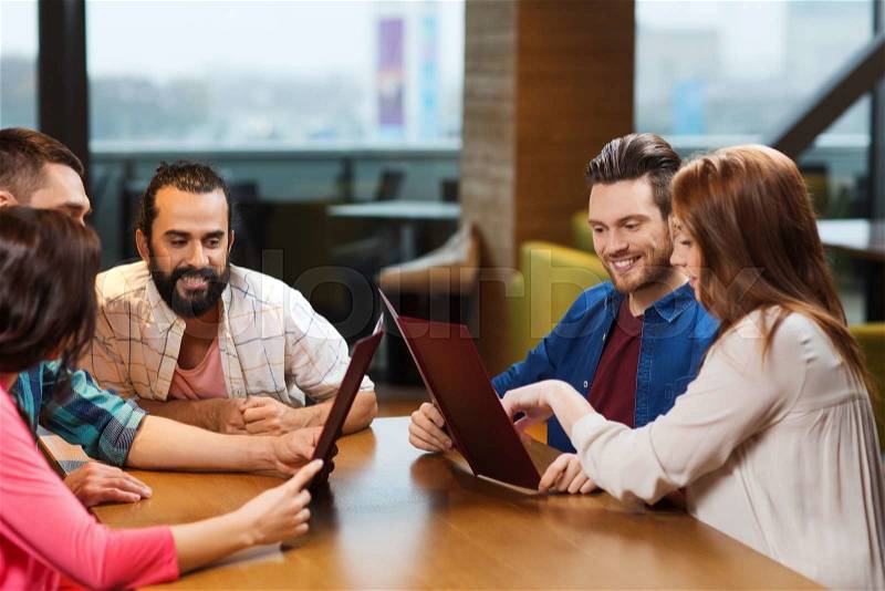 Leisure, people and holidays concept - smiling friends discussing menu at restaurant, stock photo