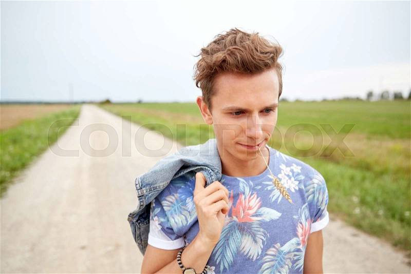 Nature, summer, youth culture and people concept - sad young hippie man walking along country road chewing rye spike, stock photo