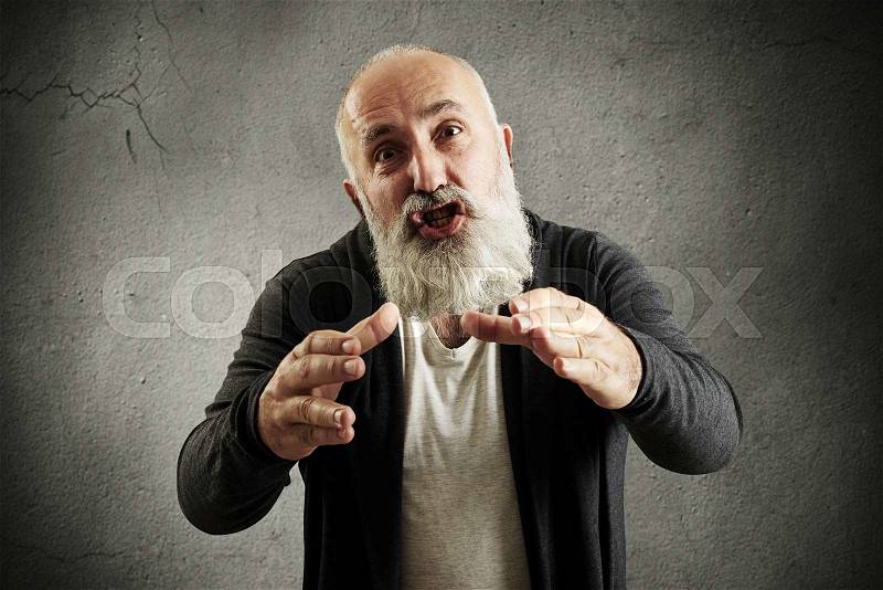 Emotional bearded man screaming, stretching his hands to camera and want to smother someone over grey wall, stock photo