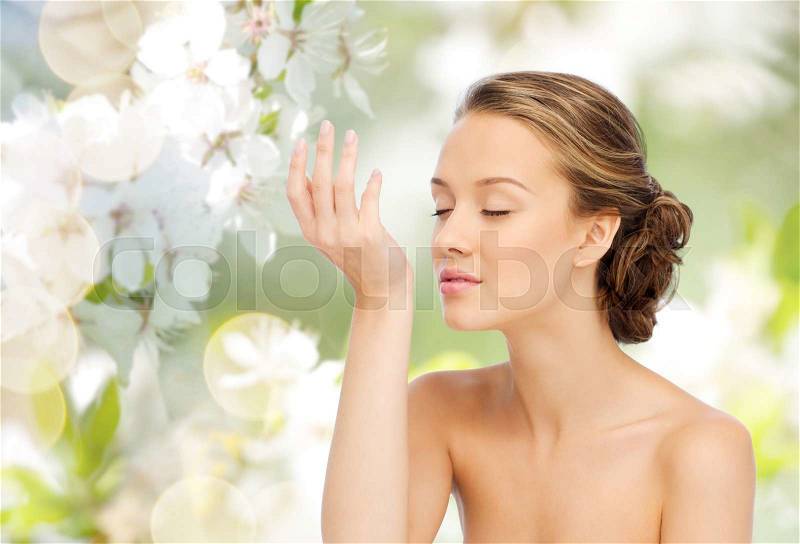 Beauty, aroma, people and body care concept - young woman smelling perfume from wrist of her hand over green natural background with cherry blossoms, stock photo