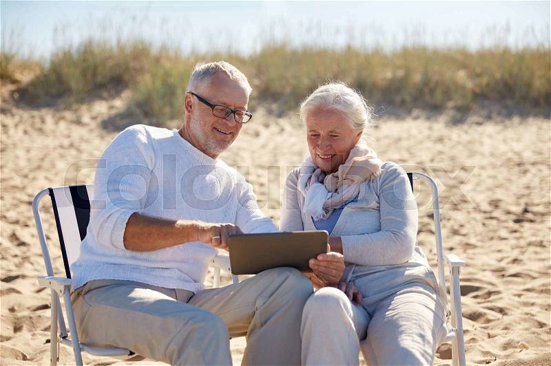 Family, age, travel, tourism and people concept - happy senior couple with tablet pc computer resting in folding chairs on summer beach, stock photo