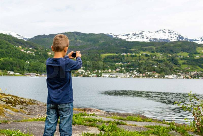 Young boy in Norway taking a picture of the surrounding scenery with his compact digital camera, stock photo