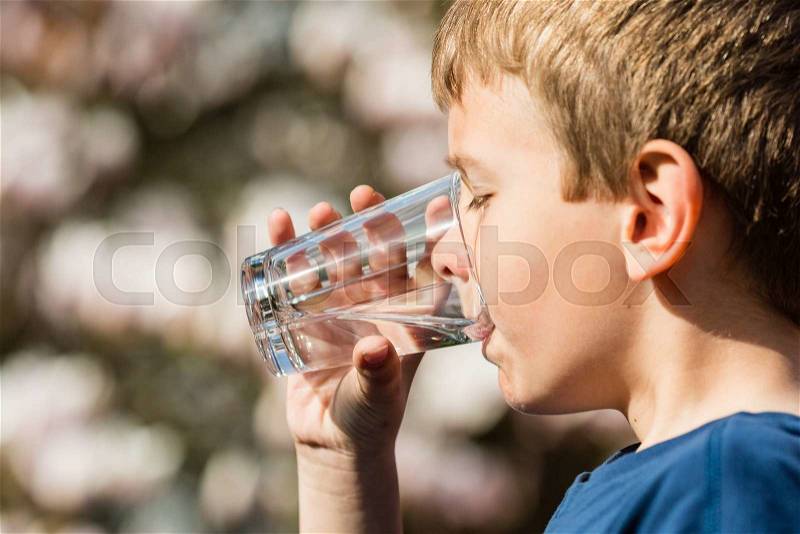 Young boy drinking from glass of fresh water. Ideal for environmental protection or future generations concept, stock photo