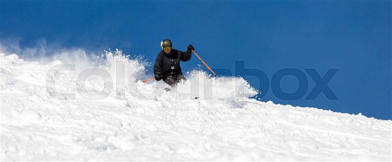 Male skier skiing off piste in powder snow a sunny winter day, stock photo