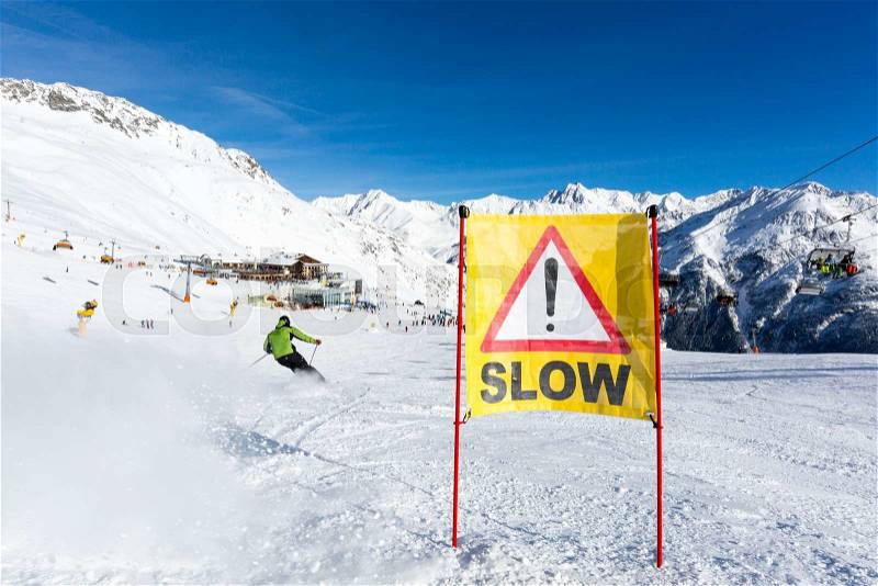Yellow slow down warning sign placed in the snow on the piste at the ski resort Soelden in Austria, stock photo
