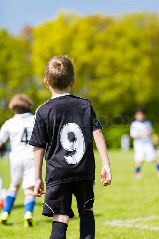 Young boy watching his team mates play a kids soccer match on soccer field with green grass, stock photo