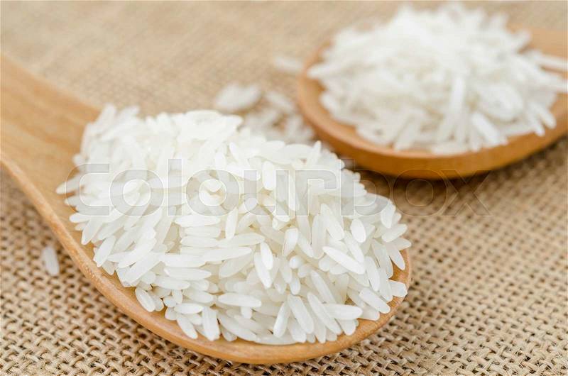 Raw rice in wooden spoon on sack background, stock photo