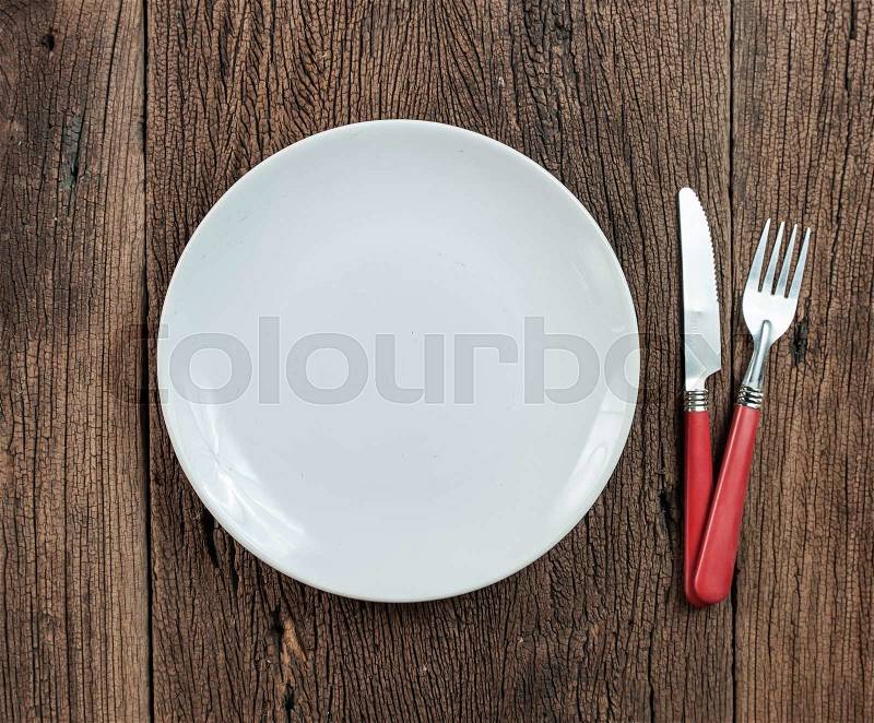 Empty white plate with silverware on wooden table. View from above, stock photo