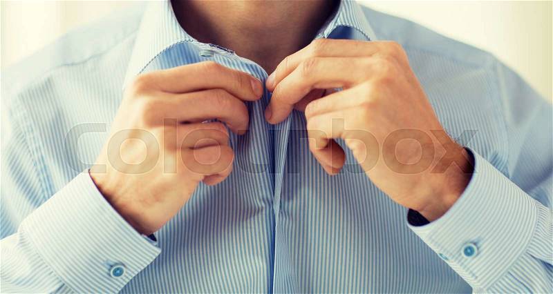 People, business, fashion and clothing concept - close up of man dressing up and fastening buttons on shirt at home, stock photo
