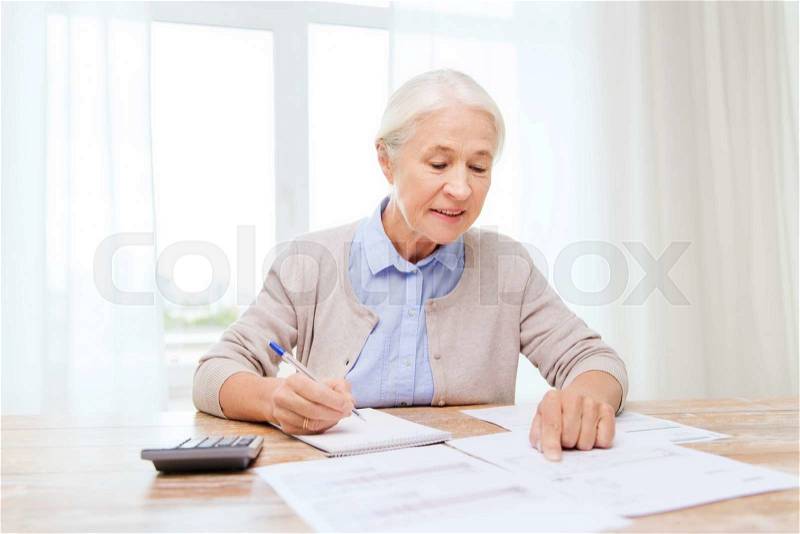 Business, savings, annuity insurance, age and people concept - senior woman with papers or bills and calculator writing at home, stock photo