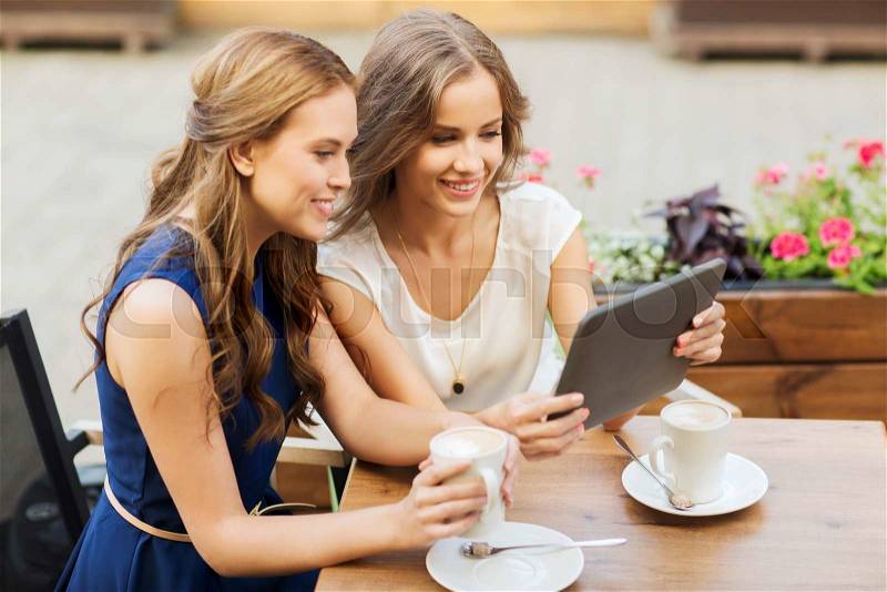Technology, lifestyle, friendship and people concept - happy young women or teenage girls with tablet pc computer drinking coffee at outdoor cafe, stock photo