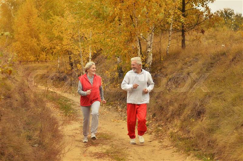 Happy fit senior couple jogging in autumn park, stock photo