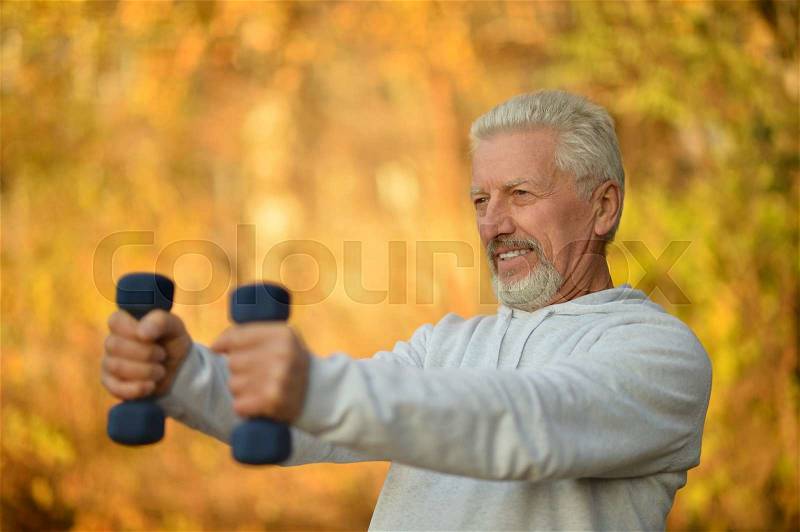 Elderly man exercising with dumbbells in autumn park, stock photo