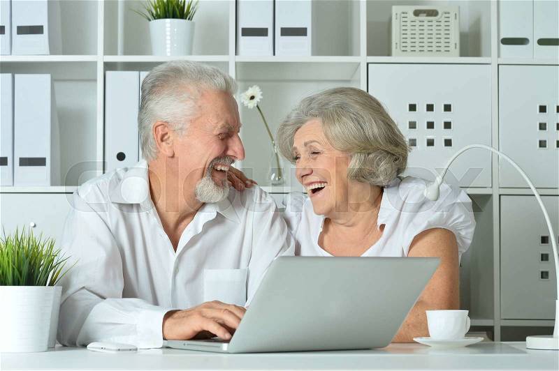 Happy senior couple with laptop in office, stock photo