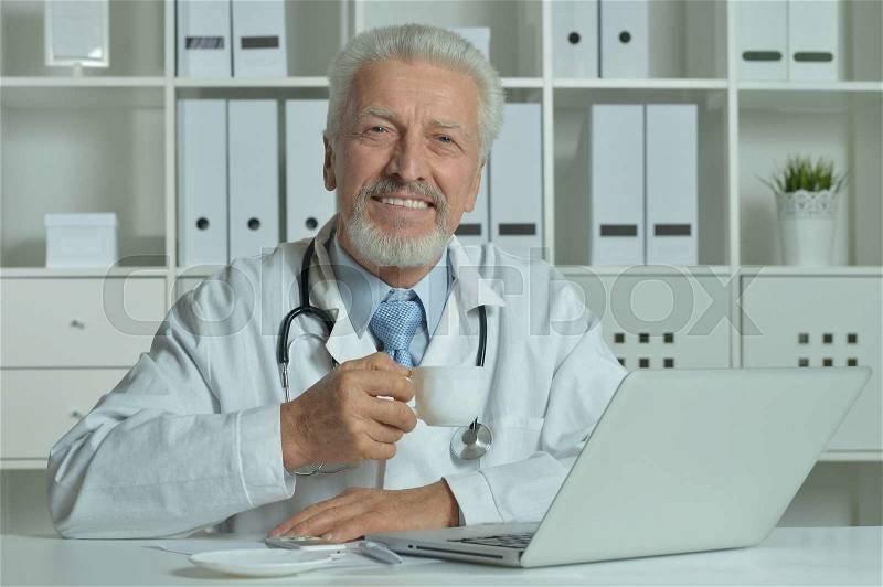 Elderly doctor with a laptop in office, stock photo
