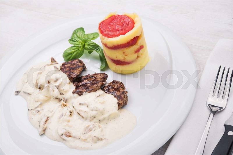 Roasted medallions with mushroom sauce, tomato and basil on white wood background, stock photo