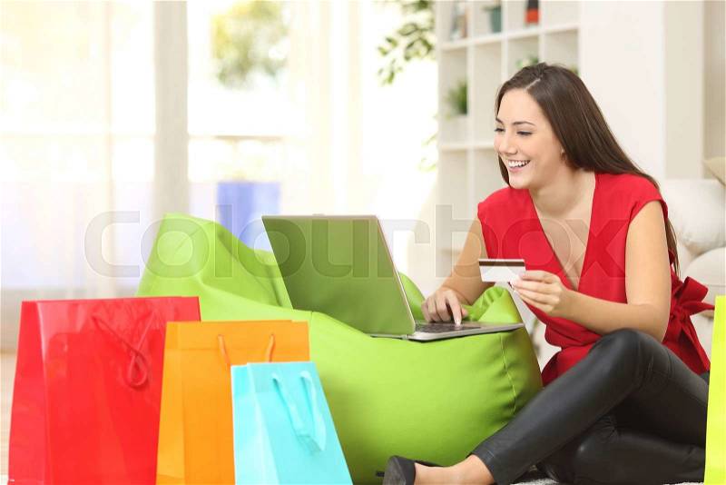 Woman buying online at home with a credit card and multiple shopping bags beside, stock photo