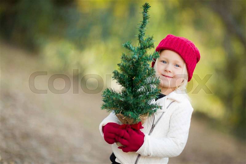 Baby Girl In Red Mittens and Cap Holding Small Christmas Tree Outdoors, stock photo