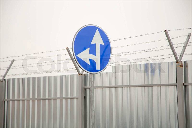 A closeup of straight and left turn arrow sign at the construction fence around airport, stock photo