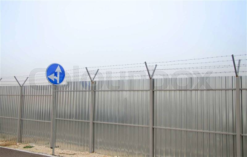 A closeup of straight and left turn arrow sign at the perimeter with barbed wire and construction fence around airport, stock photo