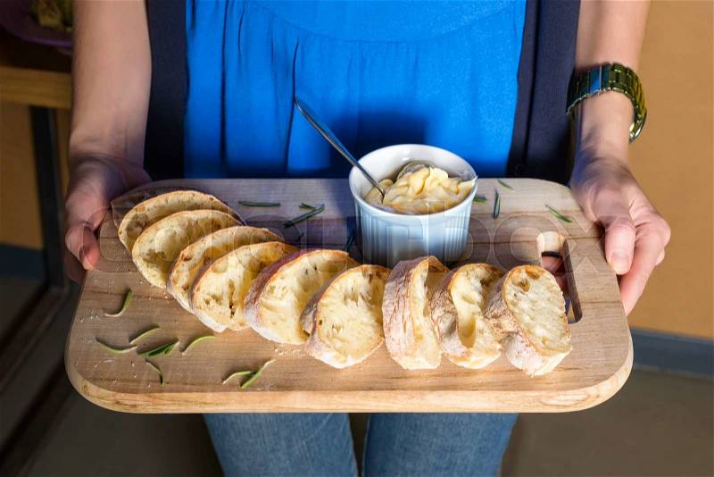 Server holding wooden tray with freshly baked bread and homemade butter. Women\'s hands with wooden server of appetizers, stock photo