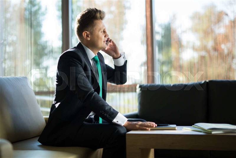 Business man in a dark suit talking on the phone. In the lobby of the hotel sitting on the couch, stock photo