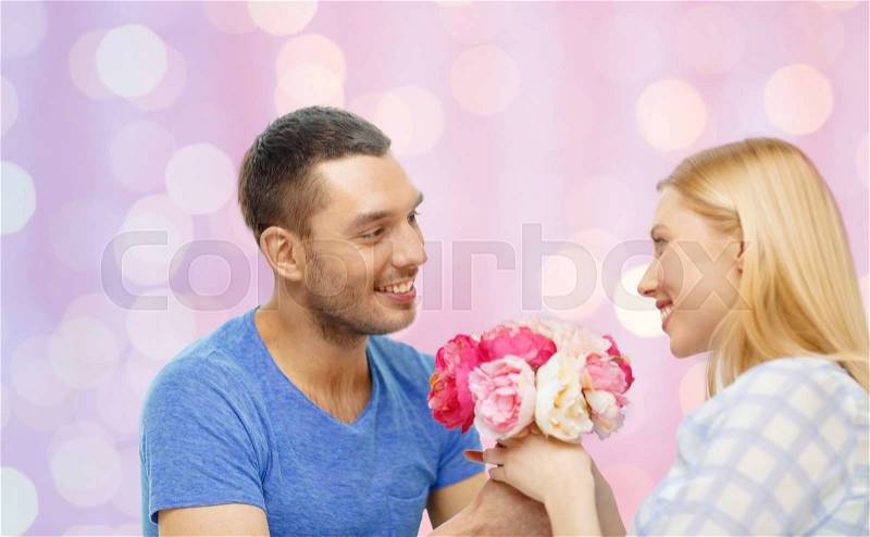 Love, holidays, valentines day and relations concept - smiling man giving woman flowers at home over pink lights background, stock photo