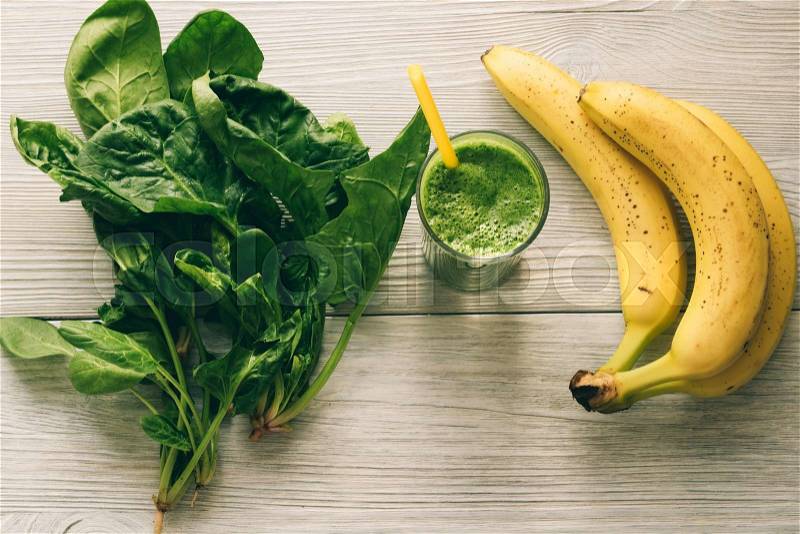 Smoothies with a straw, a banana and spinach leaves on white wooden background. The view from the top, stock photo