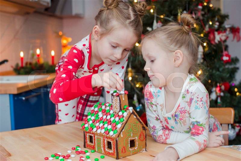 Little adorable girls decorating gingerbread house for Christmas at home, stock photo