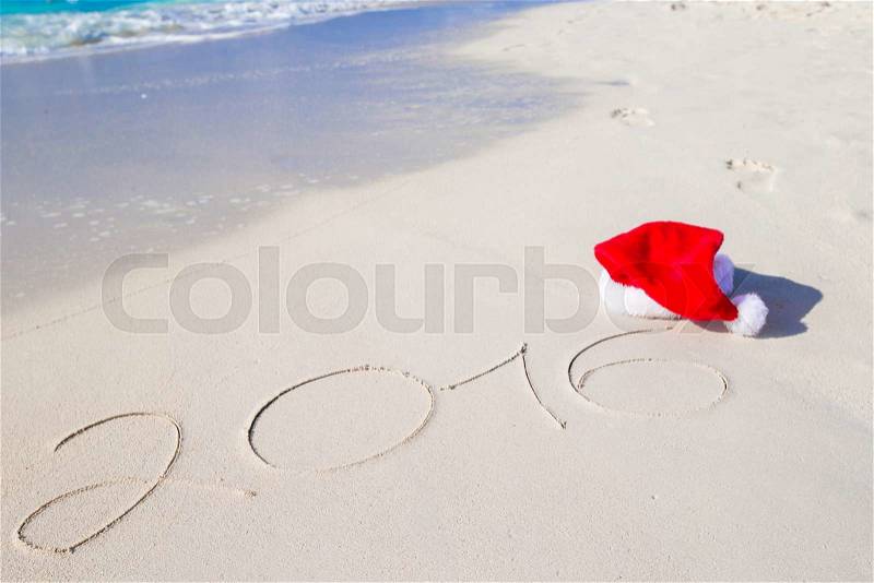 2016 and Merry Christmas written on beach white sand with red Santa hat, stock photo