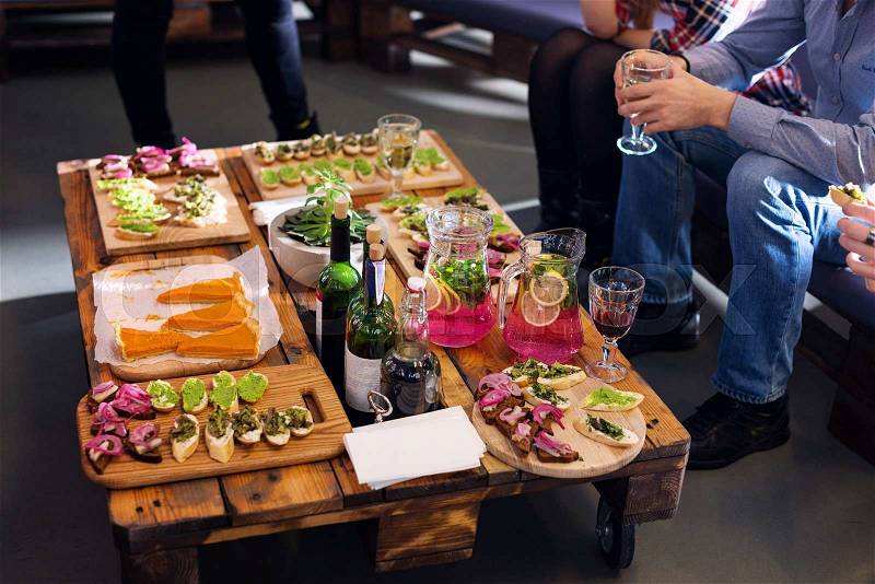 Company of friends eating together in the restaurant. Wooden tray of appetizers at a banquet on a decorated pallet coffee table and carafes of fruity beverage with lemon and mint, stock photo