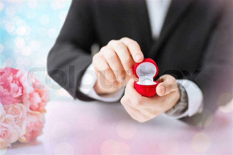 People, holidays, presents and proposal concept - close up of man with gift box and engagement ring over holidays lights background, stock photo