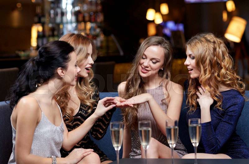 Celebration, friends, bachelorette party and holidays concept - happy woman showing engagement ring to her friends with champagne glasses at night club, stock photo