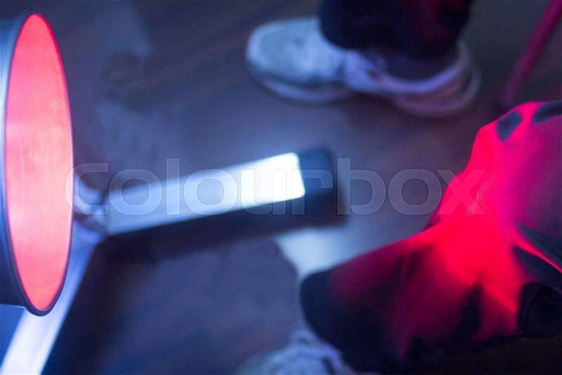 Patient leg knee joint in red physiotherapy heat treatment under hot light, stock photo