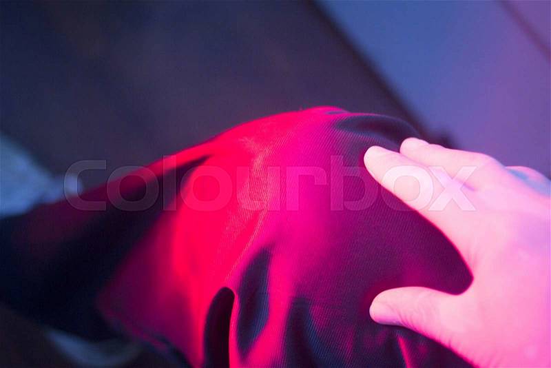 Patient leg knee joint in red physiotherapy heat treatment under hot light, stock photo
