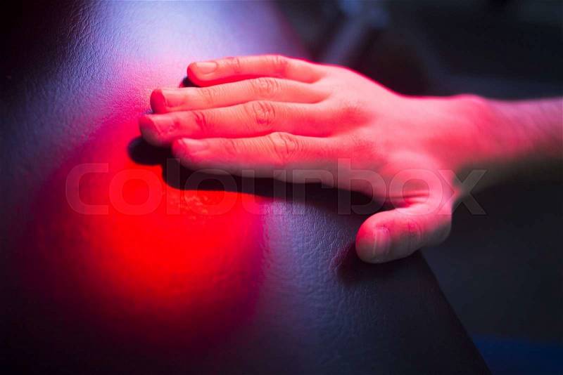 Patient hand in red physiotherapy heat treatment under hot light, stock photo