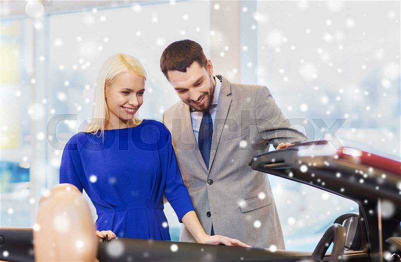 Auto business, car sale, consumerism and people concept - happy couple buying cabrio car in auto show or salon over snow effect, stock photo