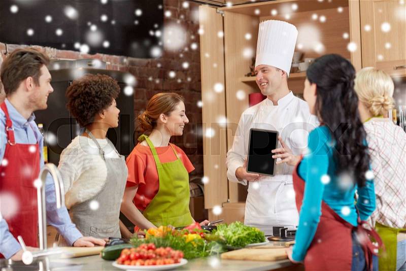 Cooking class, culinary, food, technology and people concept - happy friends with chef cook showing blank tablet pc screen in kitchen over snow effect, stock photo