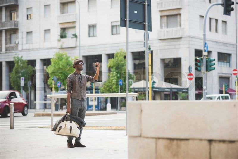 Young handsome afro black man standing in the street of the city holding a bag, taking a photo with smartphone handheld - technology, social network, communication concept, stock photo