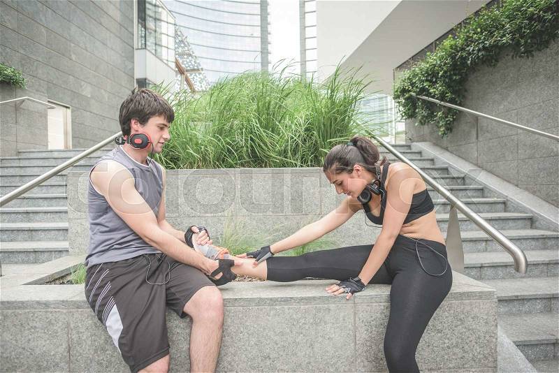 Couple of young hansome caucasian sportive man and woman helping each other stretching - he helps her to stretch her leg, both looking downward - sportive, fitness, healthy concept, stock photo
