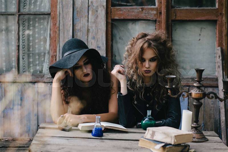 Two vintage witches perform magic ritual, with elixir in hand on the eve of Halloween, stock photo