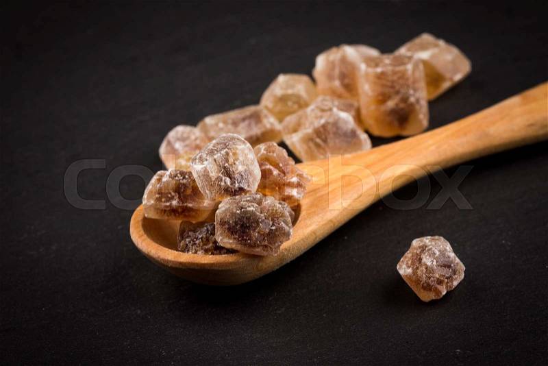 Caramelized candy brown sugar in wooden spoon on a dark stone board, stock photo