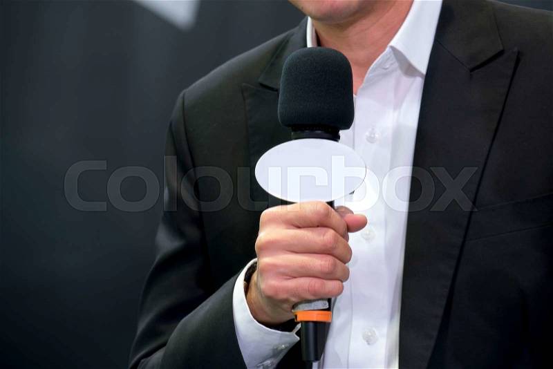 Attractive professional male news reporter holding microphone, talking to camera live broadcasting, stock photo